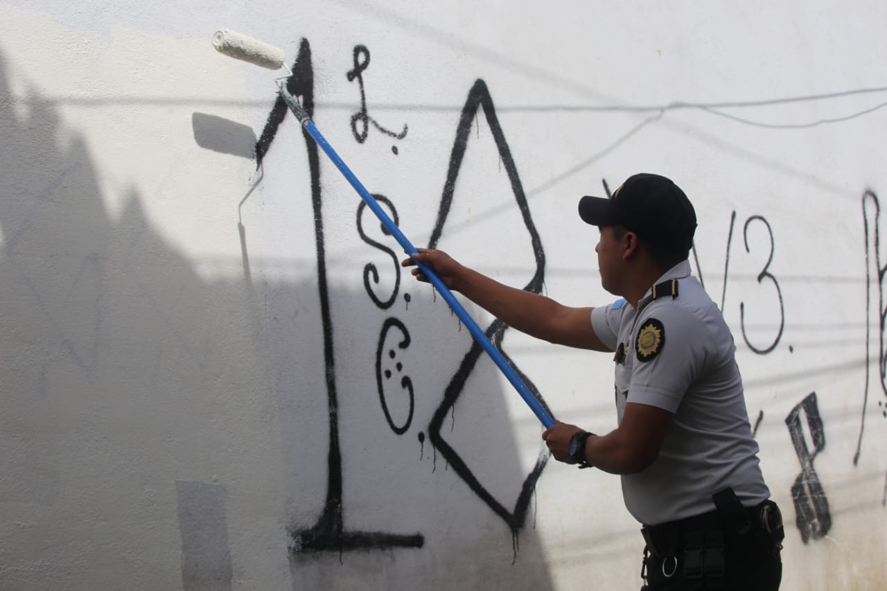 Policías borran graffittis de las pandillas en Mixco.